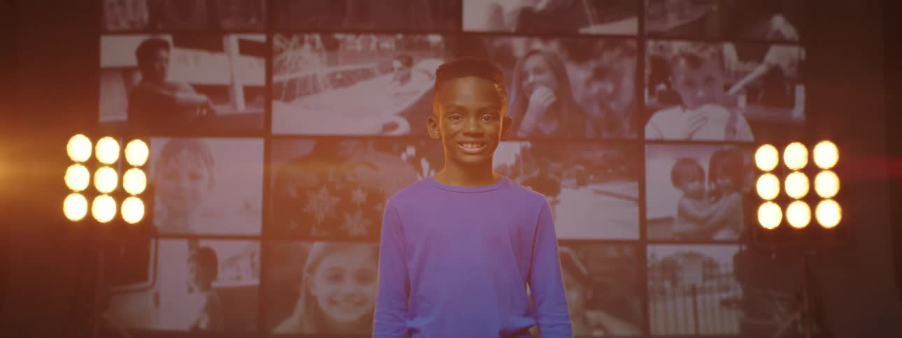 Boy stands in front of digital collage of videos bookended by light stands and smiles
