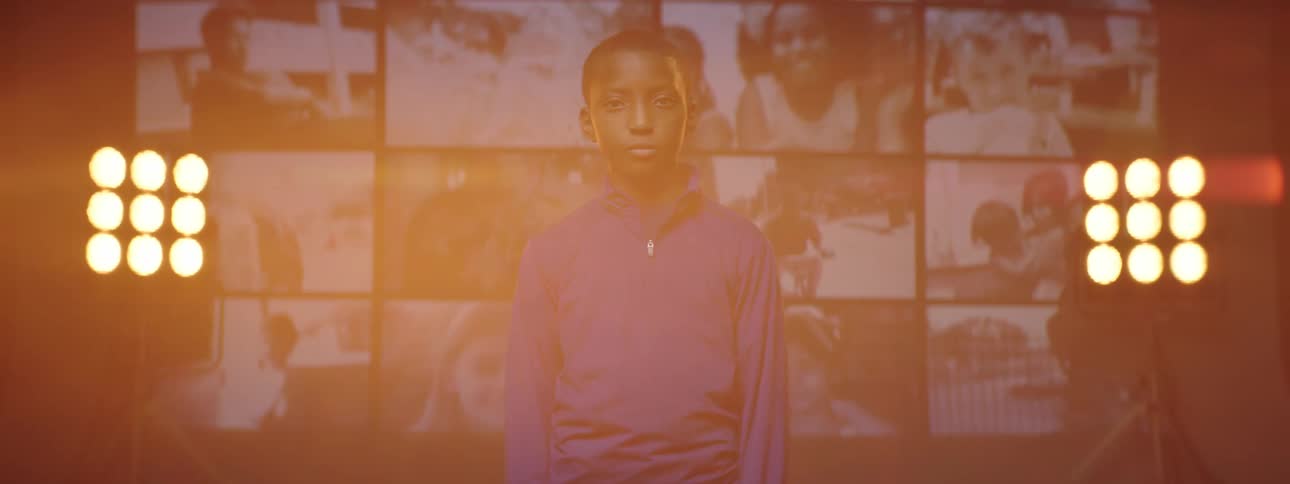 A young boy stands on a stage with screens behind him and bright lights