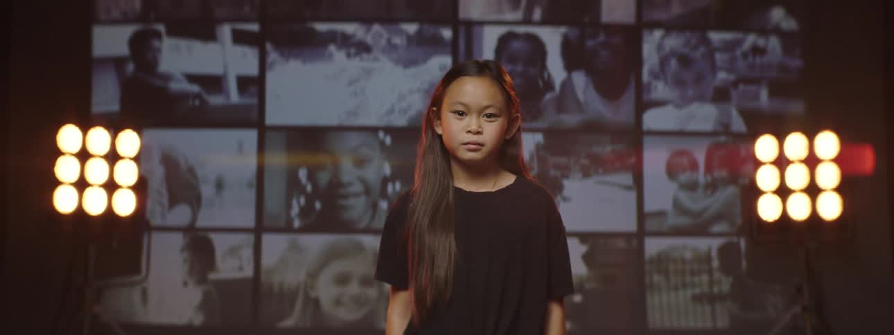 A young girl stands on a stage with screens behind her