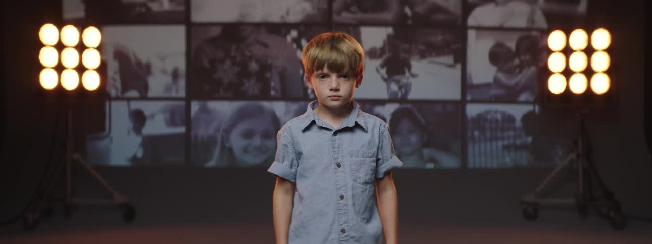 Boy standing next to panel showing videos of various children smiles