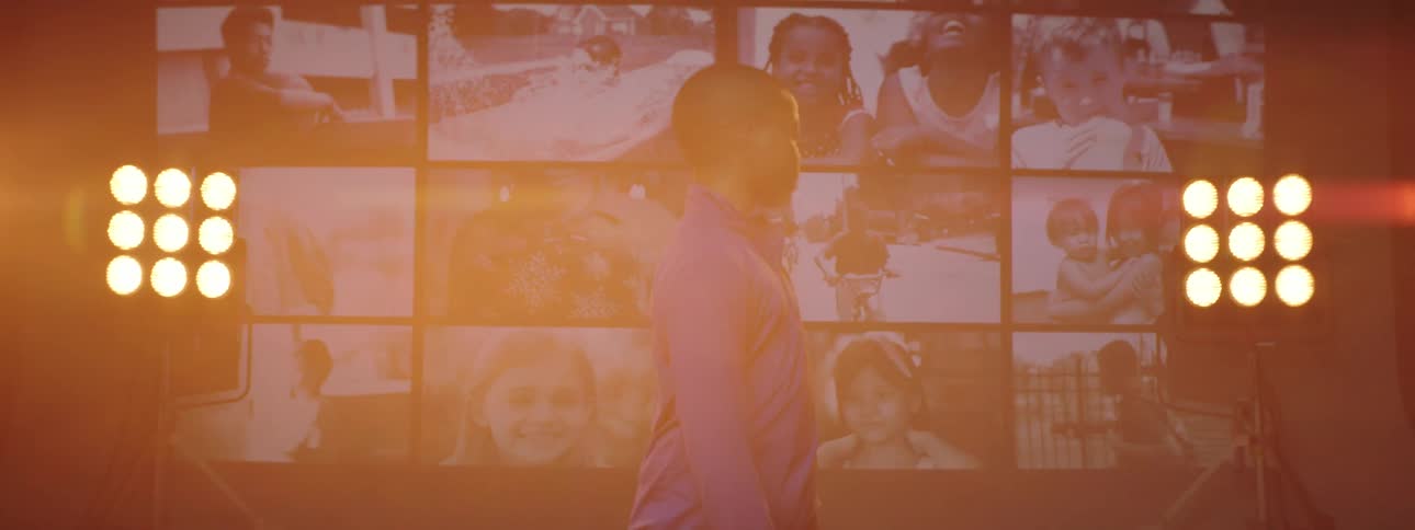 Boy with purple shirt looks over his shoulder at giant screen with kids