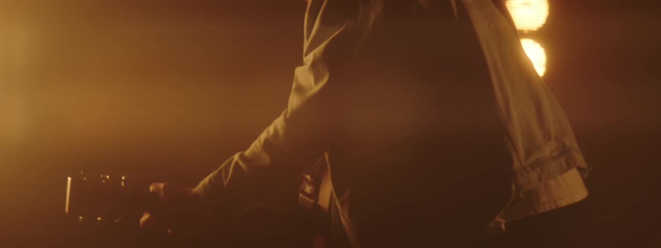 A man on a stage playing a guitar with spotlights and a wall in the background