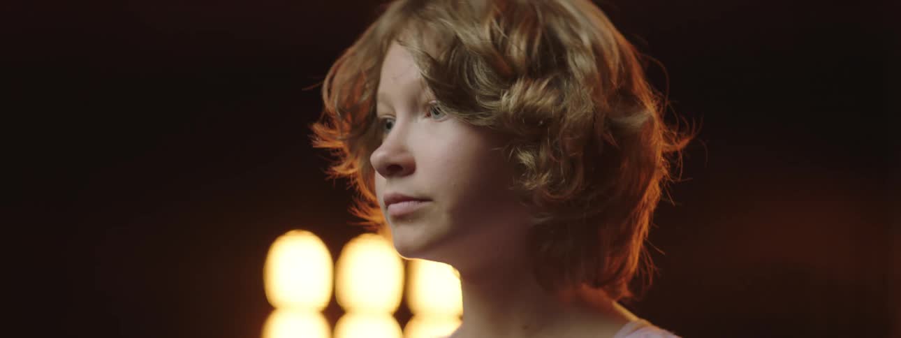 A girl raises her head while standing on stage with large stage lights