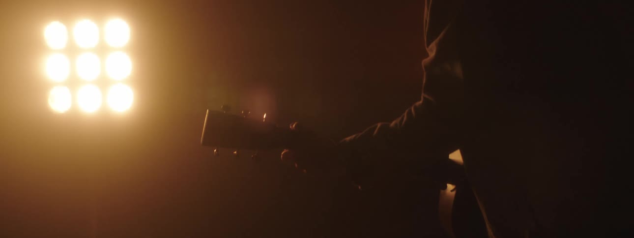 Man wearing a baseball cap plays the guitar with bright lights shining on him