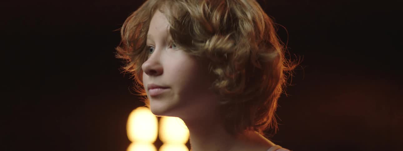A girl on stage with spotlights a screen and a wall in the background