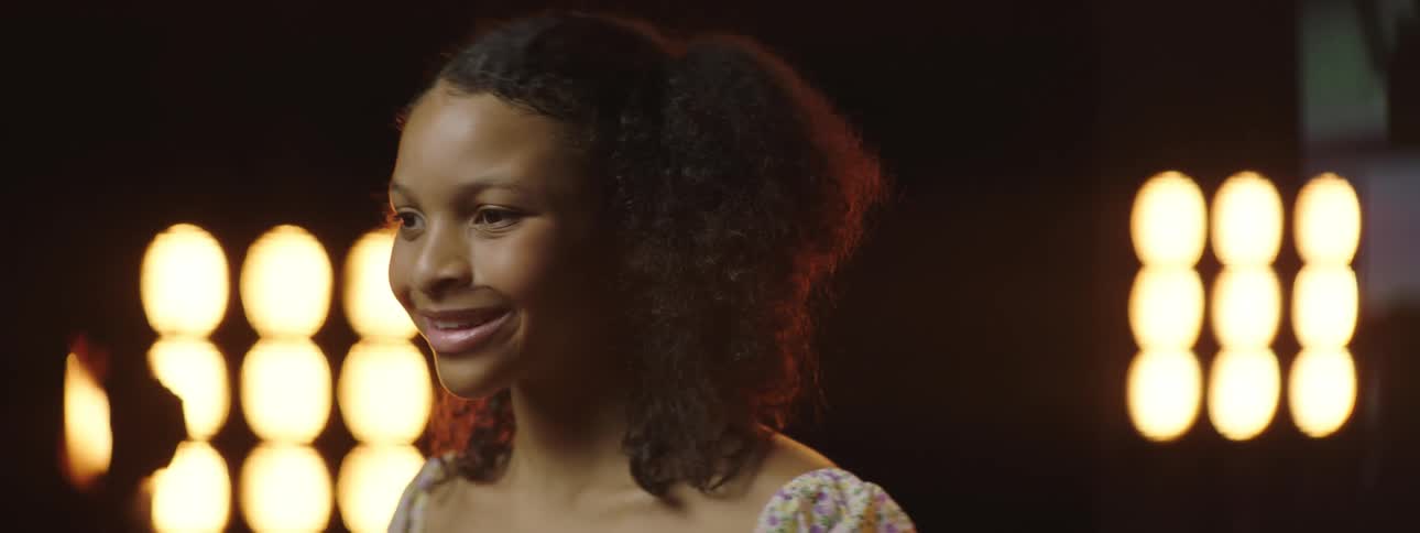 Close up of the face of a smiling girl standing on stage in front of yellow lights