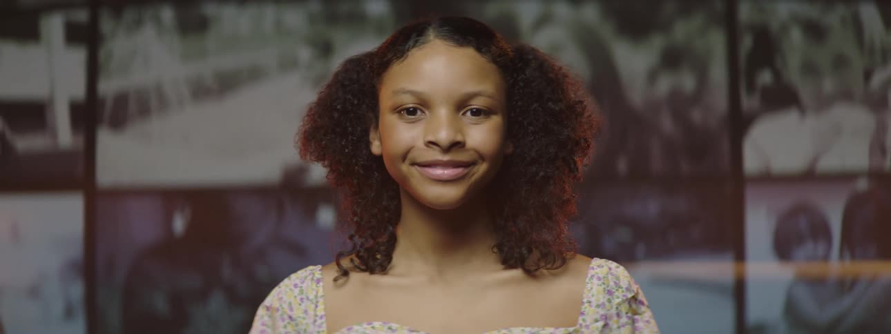 A girl standing and staring in a room with a screen and a wall in the background