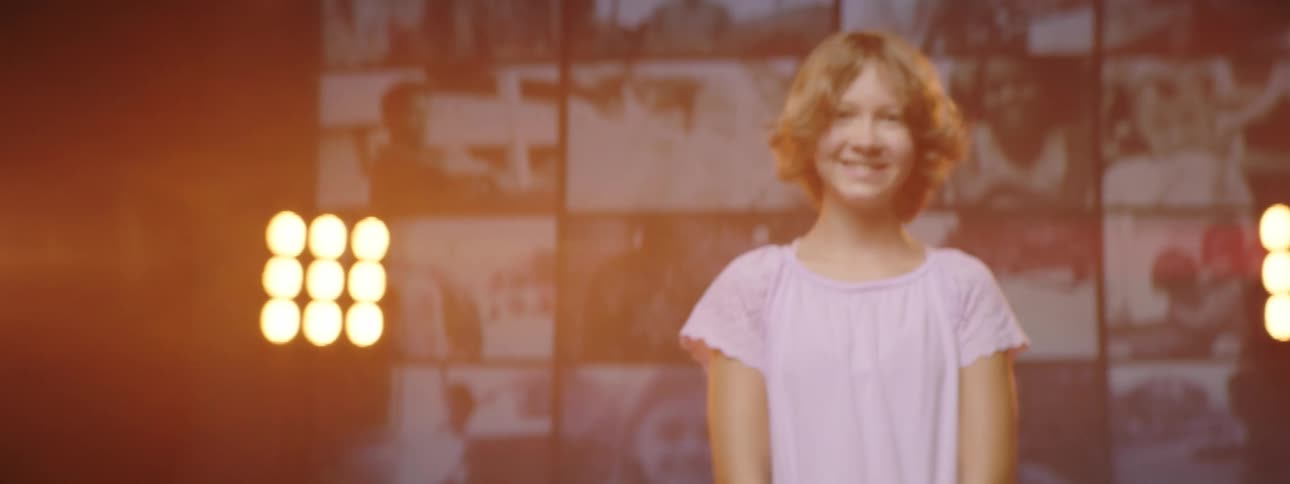 Girl standing on stage smiles while looking at the camera in front of a digital display