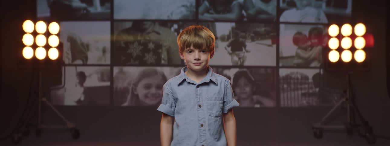 Blonde boy standing on a stage in front of a wall of photographs