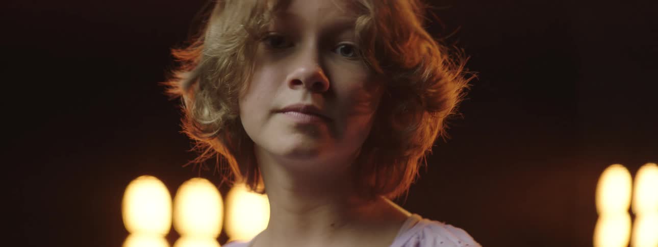 A girl with her head bowed looks up as she stands in front of a projector screen
