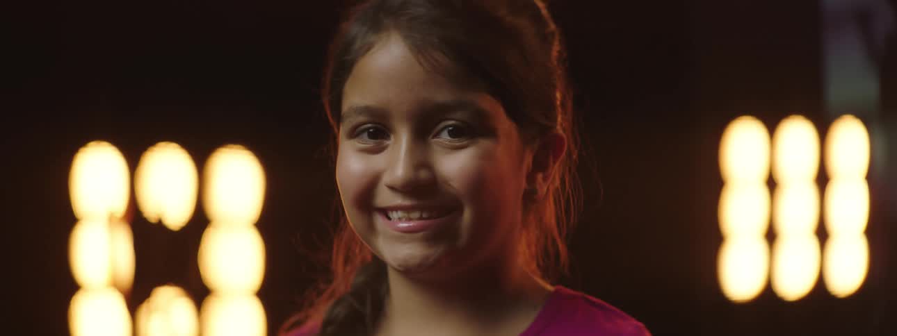A girl smiles with stage lights glowing behind her