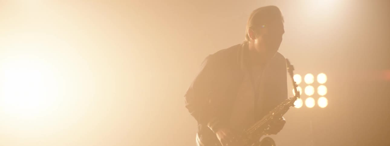 Man plays saxophone on foggy stage under stage lights