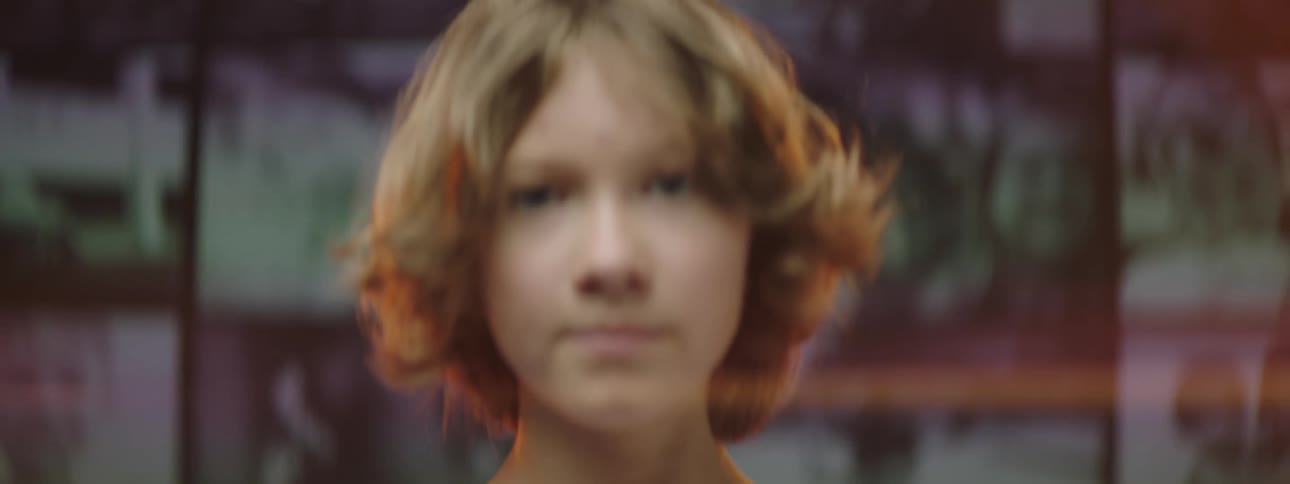 A girl turns around from watching a collage of videos playing on a large screen