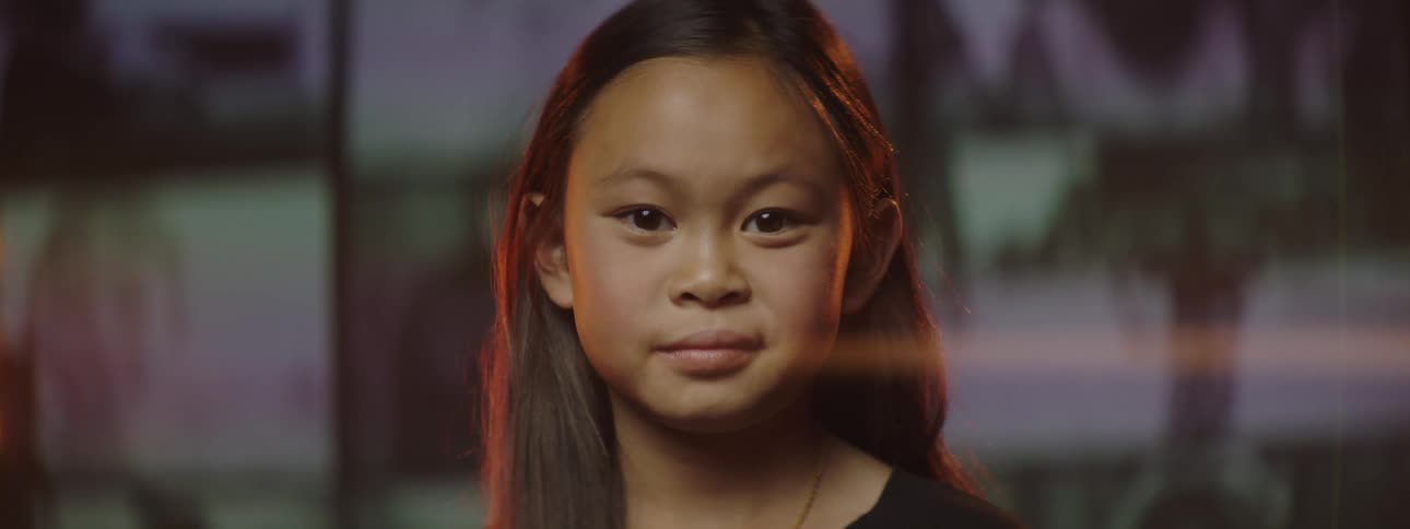 A girl goes from serious to smiling with videos playing on a wall display behind her