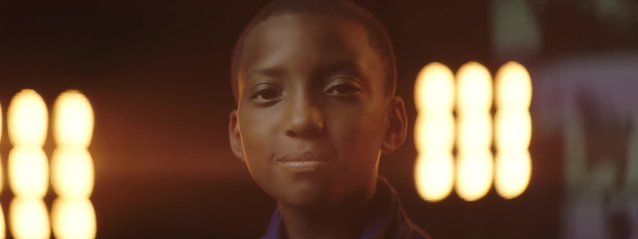 Black male teenager smiles as bright lights shine on him from behind