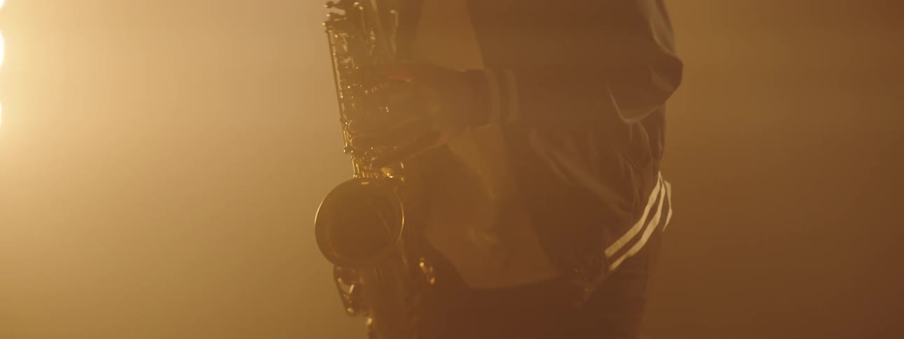 A man sways and dances as he plays the sax with stage lights behind him