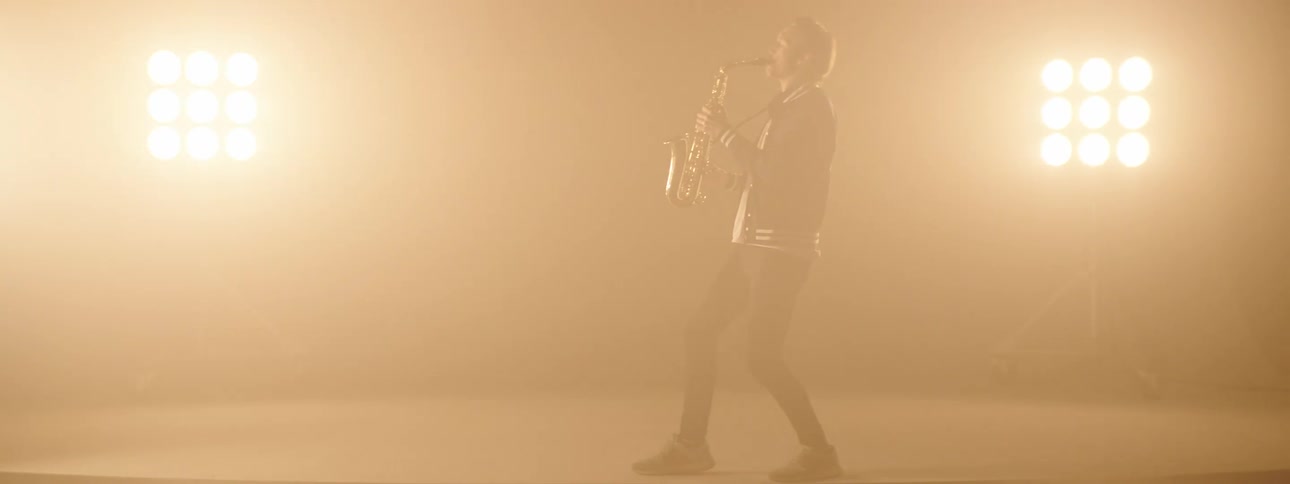 A man playing a saxophone on a stage with spotlights and a wall in the background