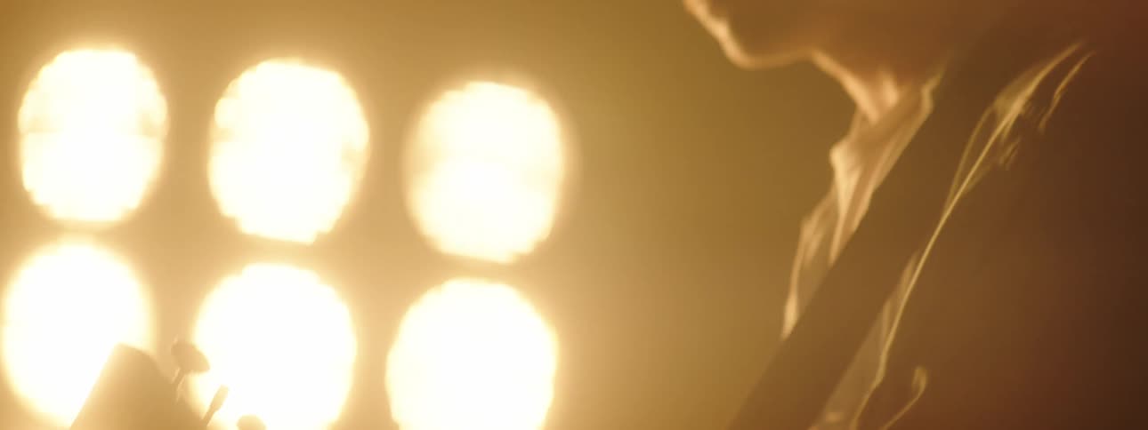 The silhouette of a man playing guitar swaying with lights shining behind