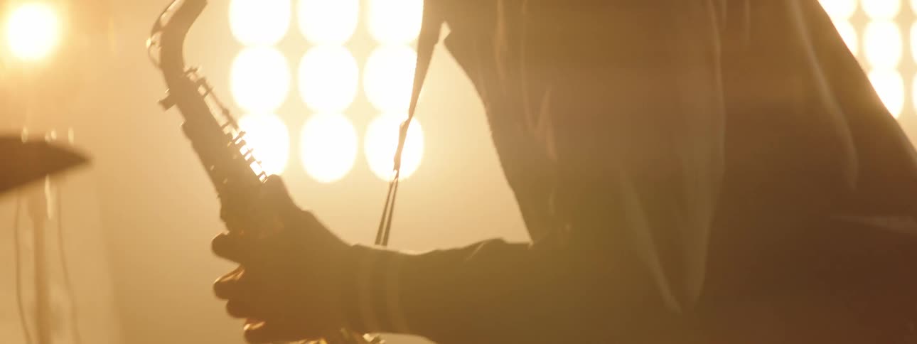 A man plays the sax in front of bright lights indoors