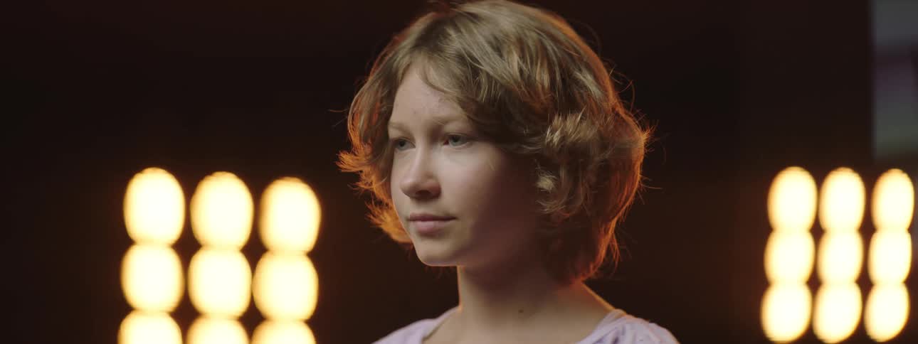 Girl with short hair stands in front of bright lights