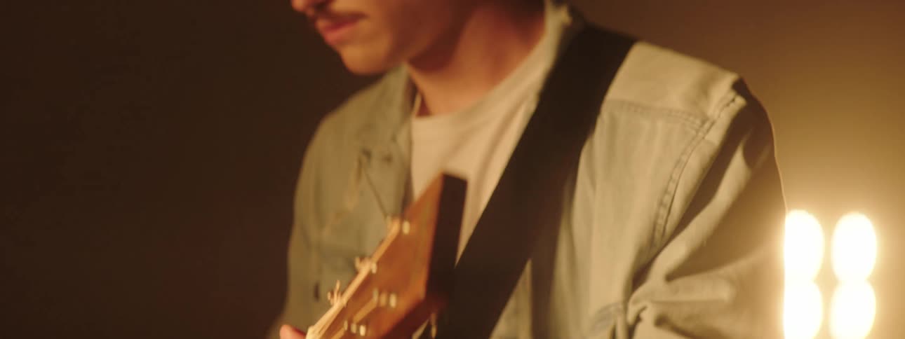 Guitarist plays acoustic guitar on stage under bright lights