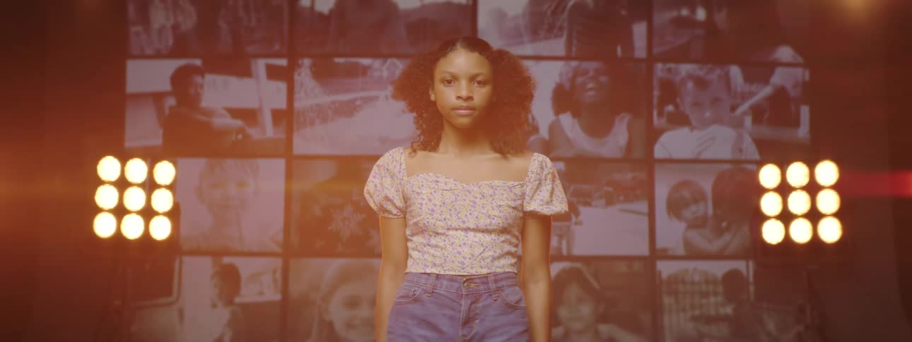 Young woman stands in front of lights and wall of screens showing various images