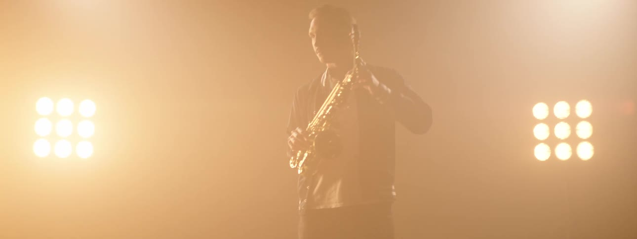 Man dances while playing the saxophone as bright lights shine on him
