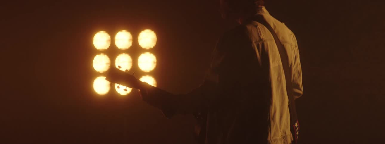 A guitarist plays the guitar on stage in front of large stage lights