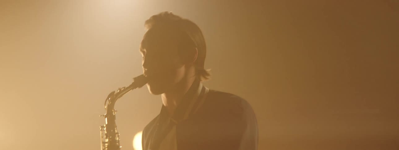 A man plays the saxophone in front of bright stage lights