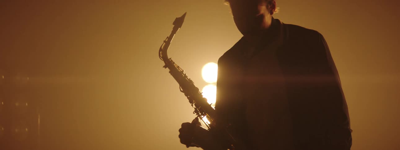 A man walks onto a dim stage holding his saxophone