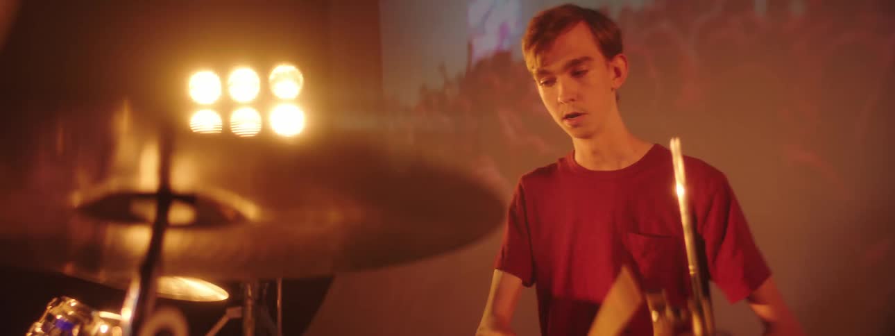 Baterist playing on a drumset on stage in front of a digital display and flashing lights