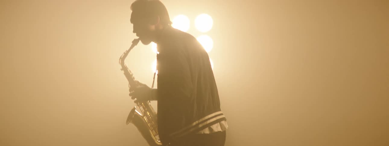 A man playing a saxophone on a stage with spotlights and a wall in the background