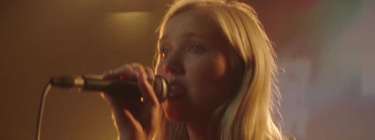A young woman holds a microphone singing on stage