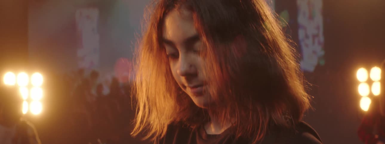 A boy with long hair plays the guitar with his band in front of a projector screen