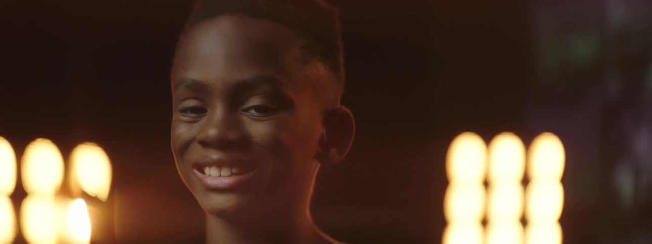 Black teenager stands in front of bright lights and smiles