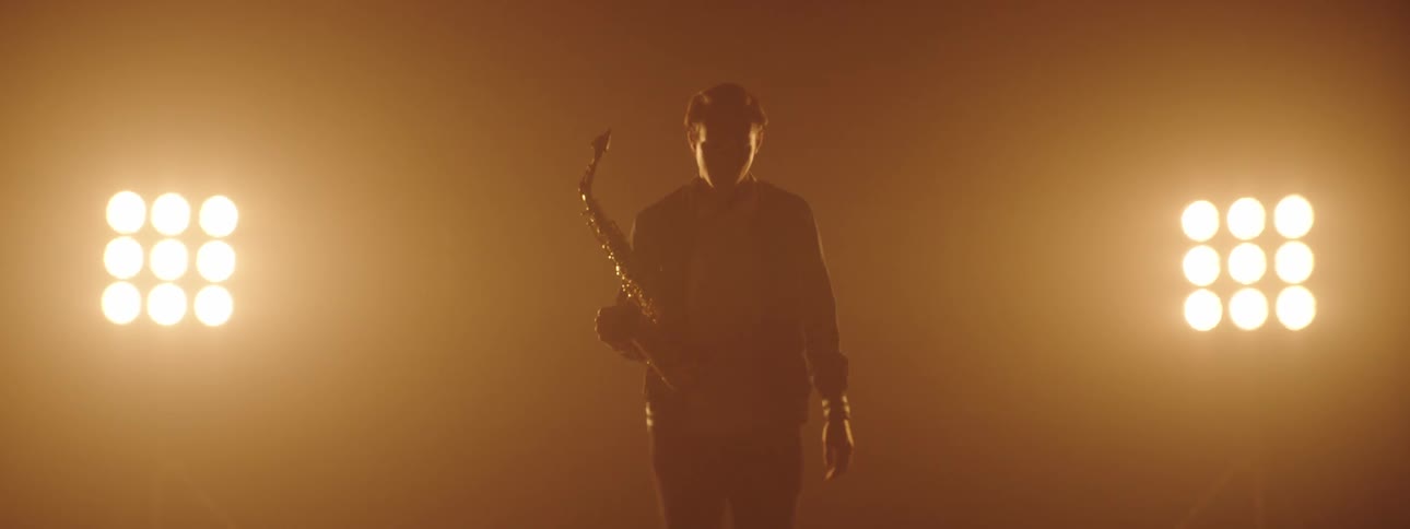A man walks onto a stage carrying a saxophone