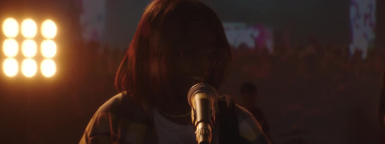 A woman sings and dances while playing guitar in a band with video playing behind her