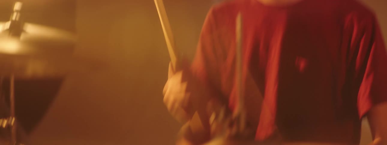 A teen bobs his head while playing drums with stage lights shining and video playing behind