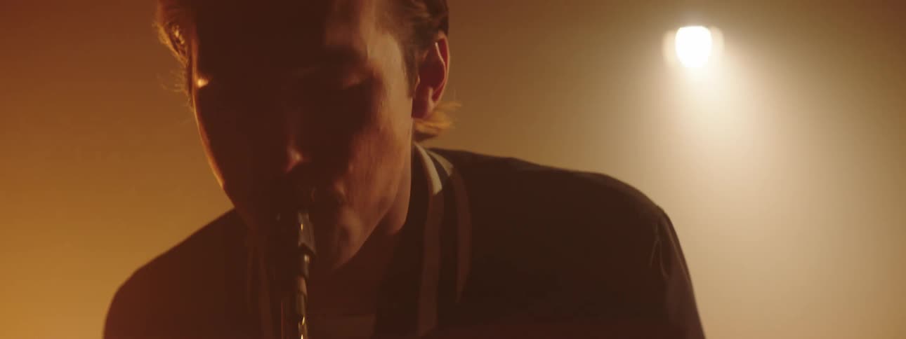 A man sways as he plays the sax with stage lights shining behind him