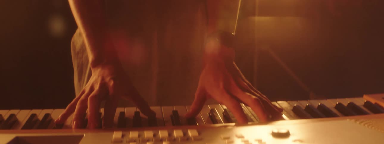 Bright stage lights shine behind a keyboard player while video of a crowd plays