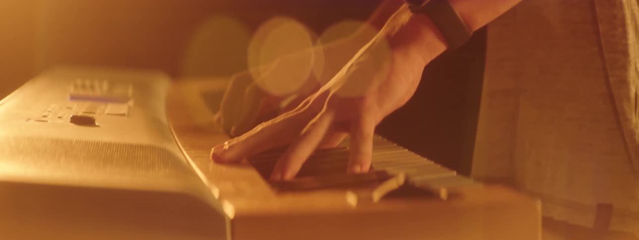 A person with a wristwatch playing a keyboard in a room with a wall in the background