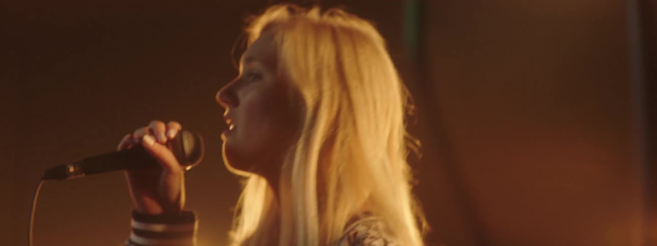 Blonde woman sings on foggy stage under bright lights during performance