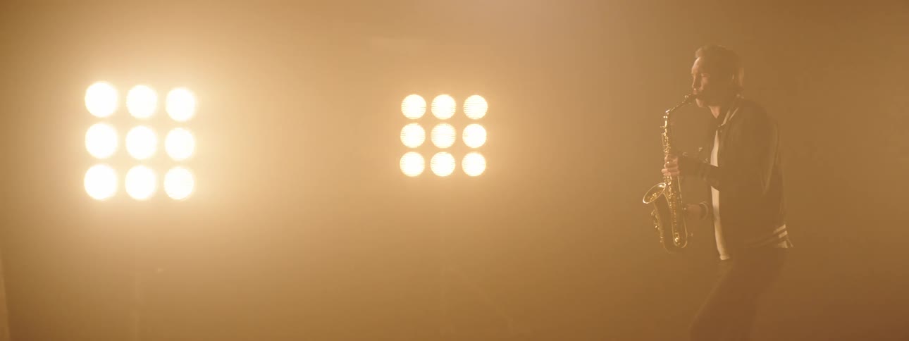 A man sways and dances while playing the sax with stage lights glaring