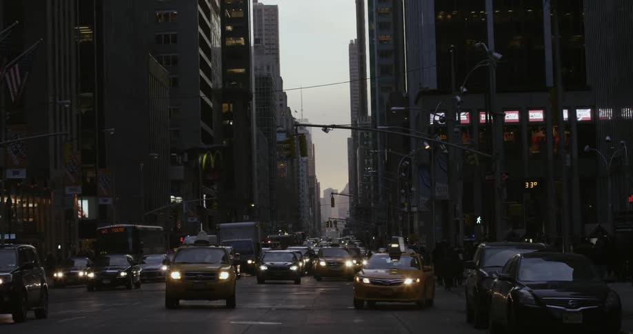Cars and buses travel down a crowded city street at dusk