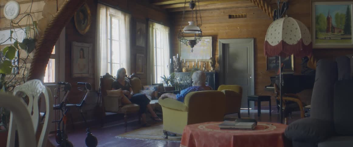 Two women in a room sitting on couches with a wall and windows in the background