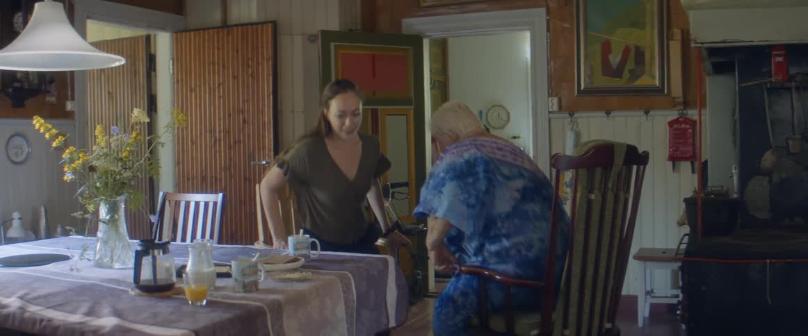 A younger woman sits down and picks up a coffee cup to hand to an elderly woman