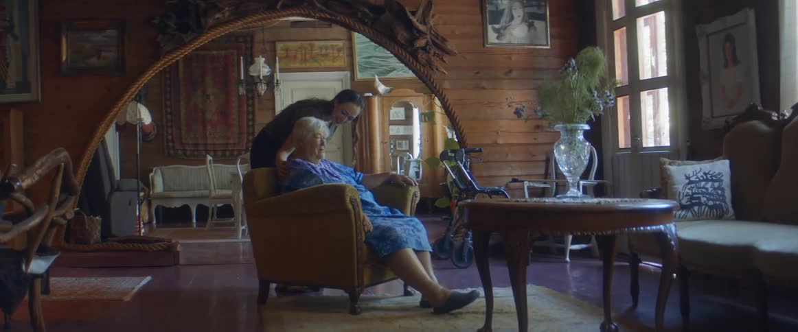 A woman checks on her mother sitting in a chair in the living room