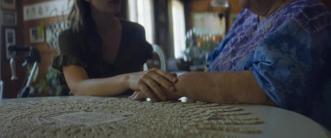 A woman holds the hand of an elderly woman and listens as they sit at a table