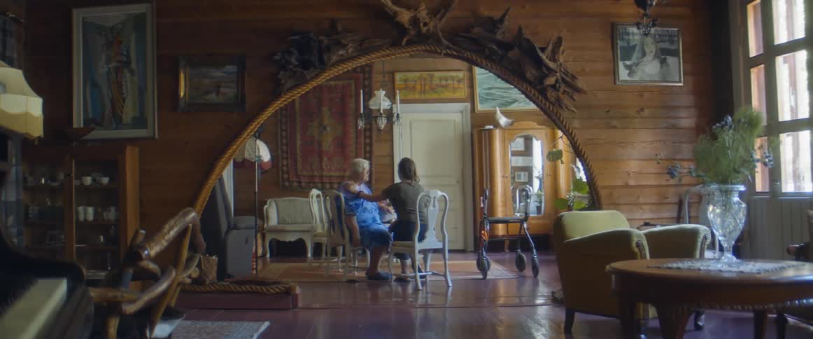 Granddaughter places her hand on her grandmothers shoulder as they sit on chairs