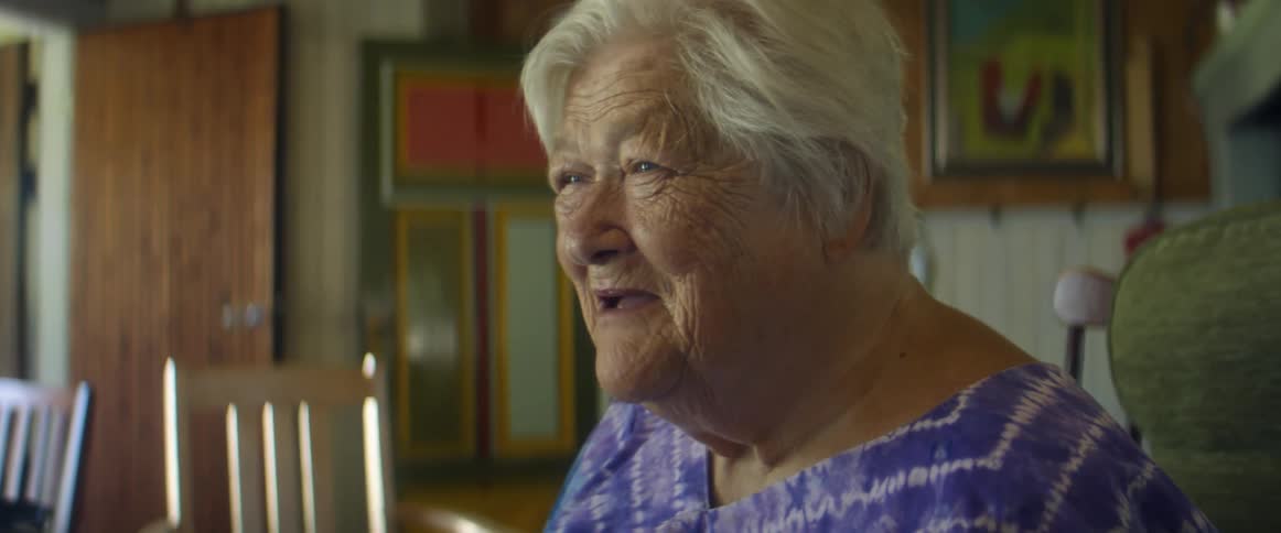 Elderly woman with grey hair and blue eyes talks with young woman in the living room